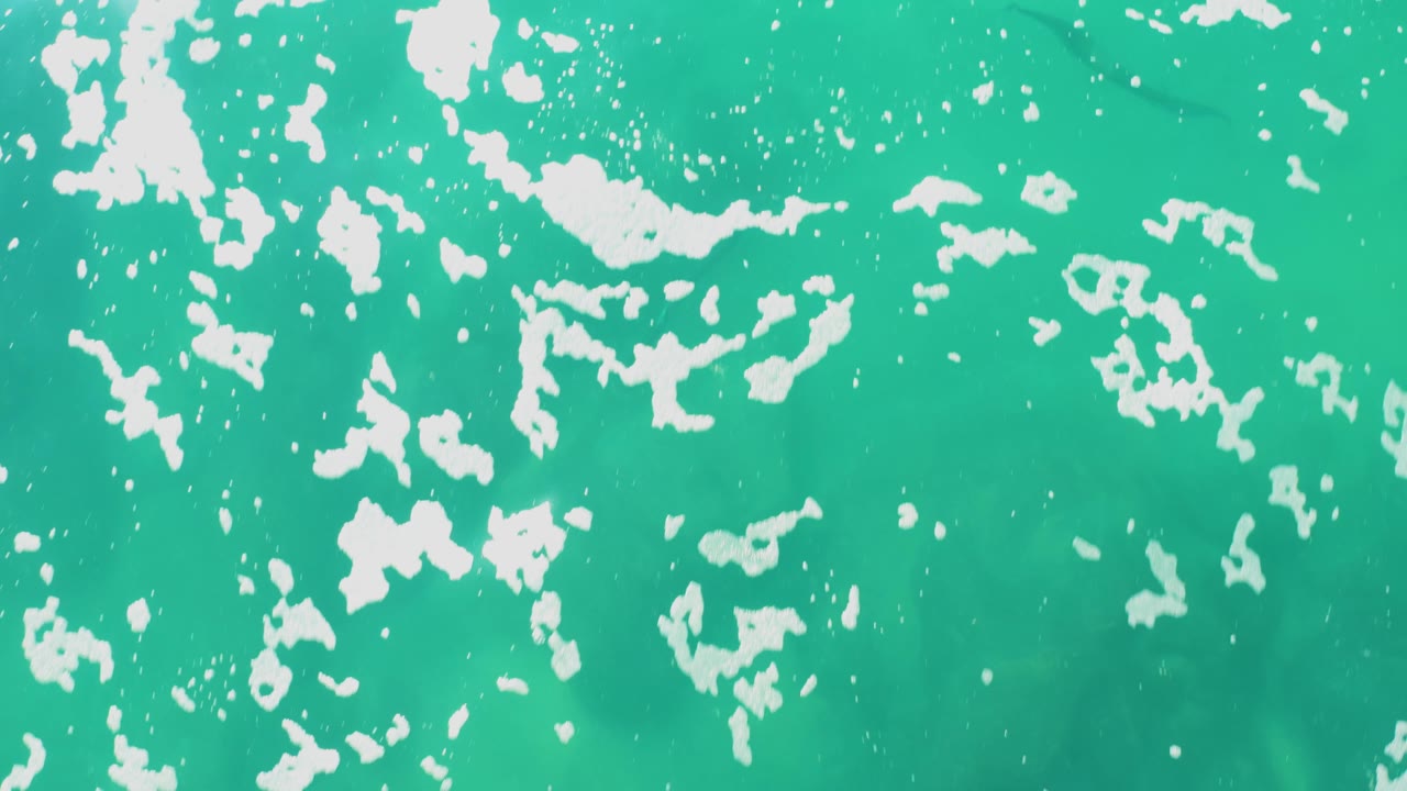 Turquoise ocean surface with scattered white foam patches.