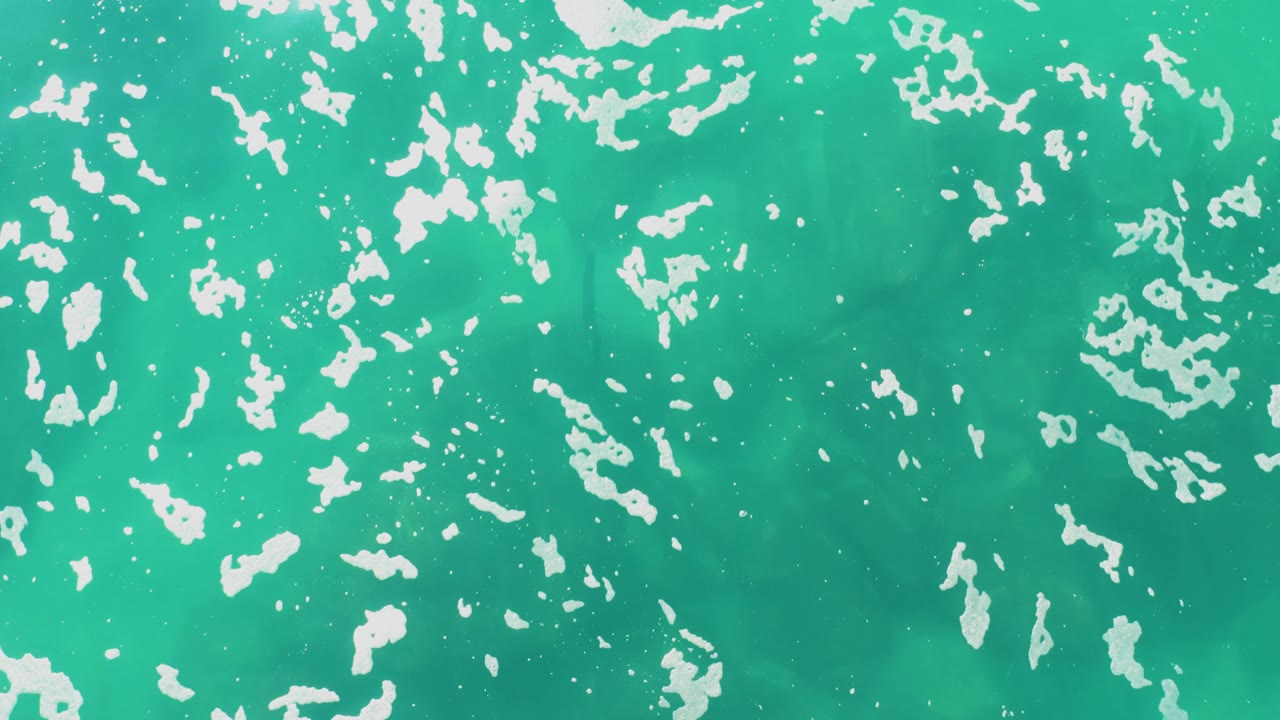 At two seconds, broken white foam shapes are dispersed over turquoise ocean water at Laguna Beach Los Cabos, and no people or objects are visible.