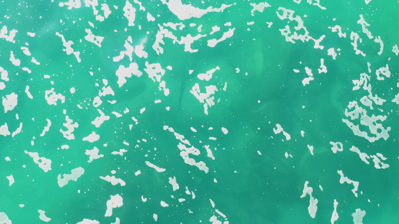 Turquoise sea surface with dense white foam patches near the top