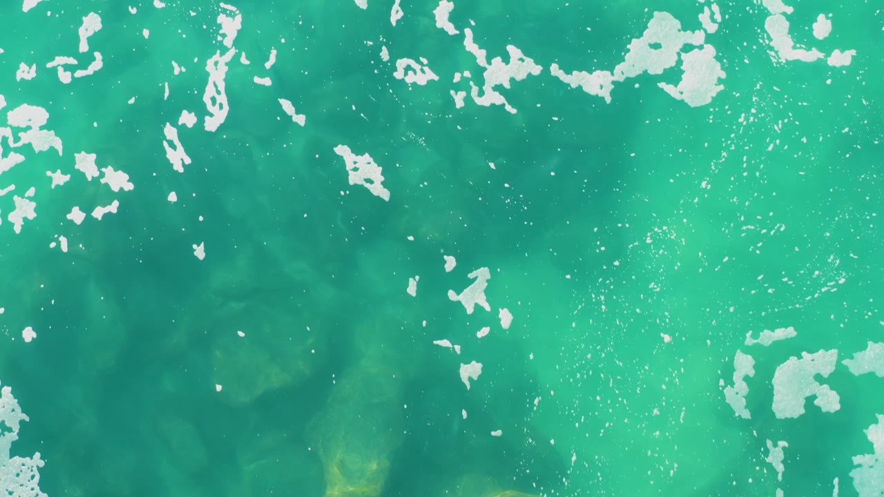 Turquoise ocean surface with scattered white foam.