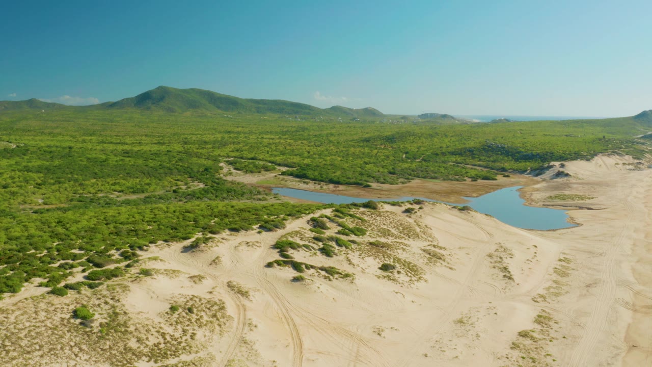 Aerial view of sand dunes and scrub with two blue water areas beside a green forest valley.