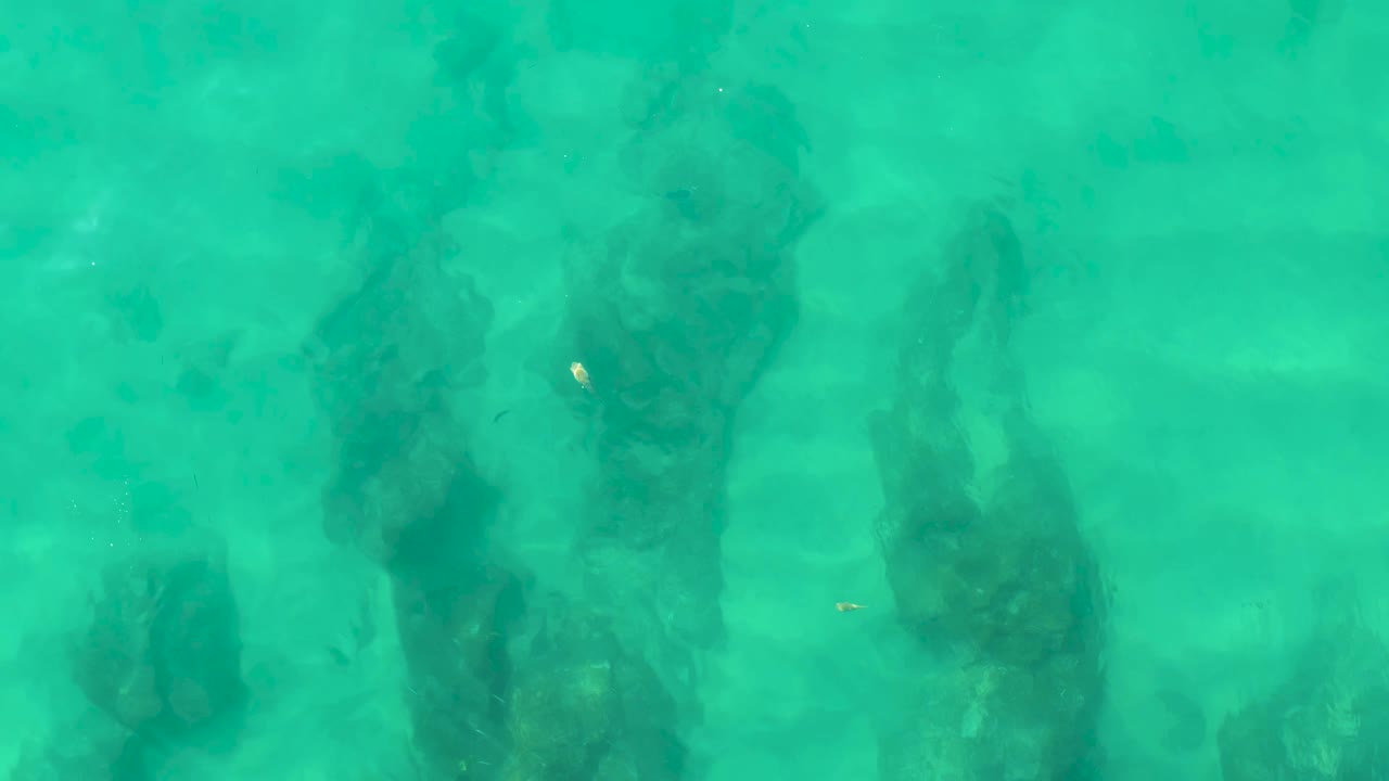Turquoise water over dark underwater rock formations.