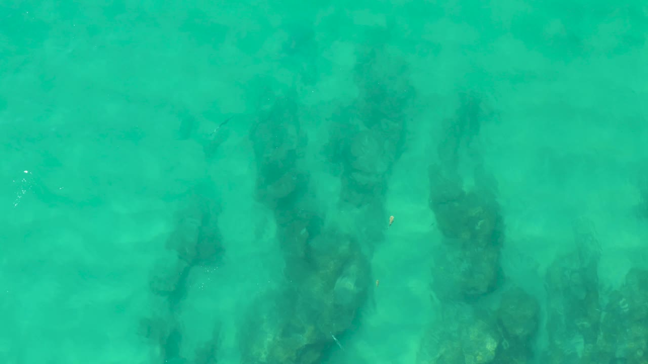 Turquoise shallow water over dark submerged rocks.