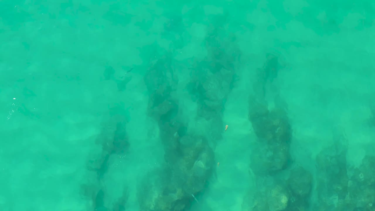 Aerial frame of clear green-blue water in Laguna Beach Los Cabos showing darker rock masses under the surface, with no visible people.