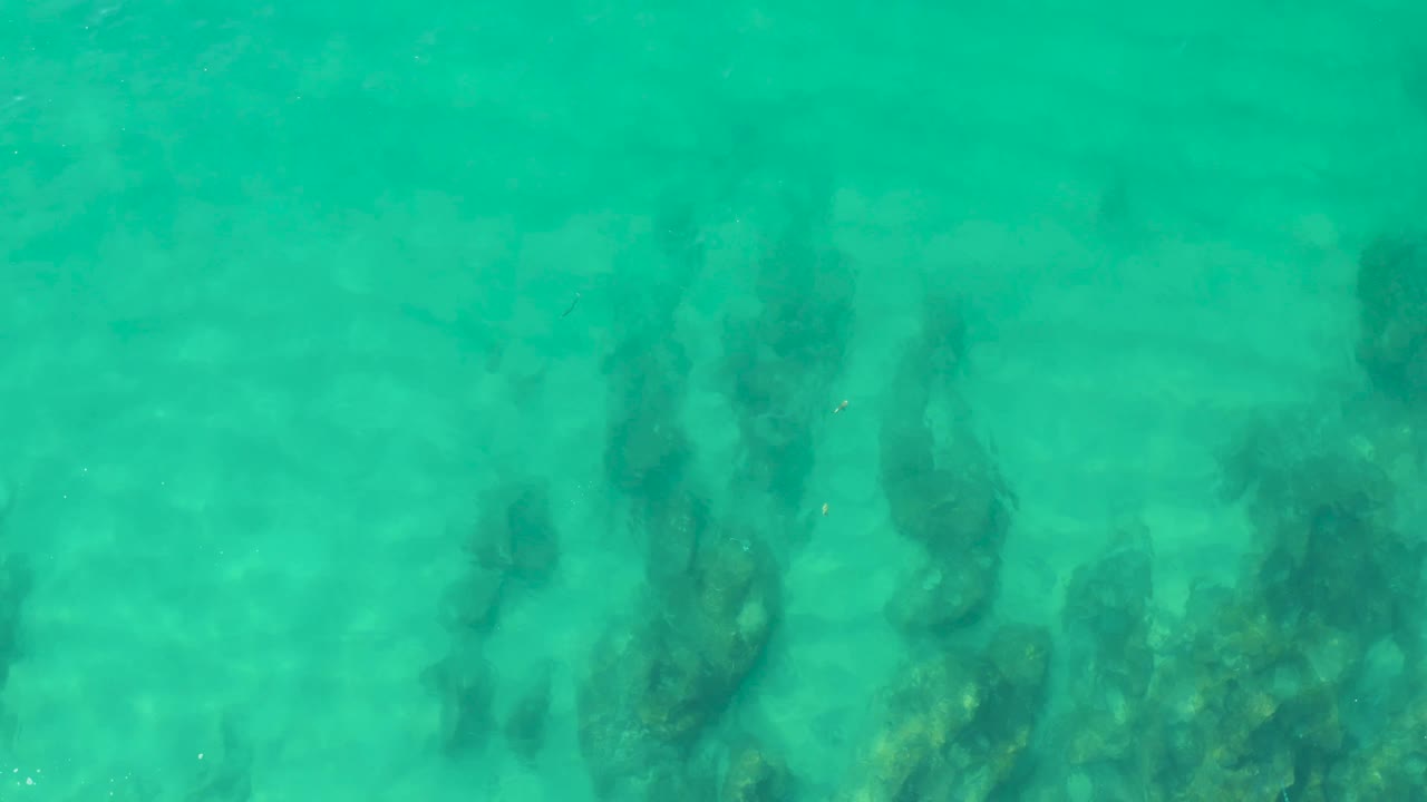 Rippling turquoise water at Laguna Beach Los Cabos passes over darker underwater rocks or coral, making the shapes less distinct, with no visible people.