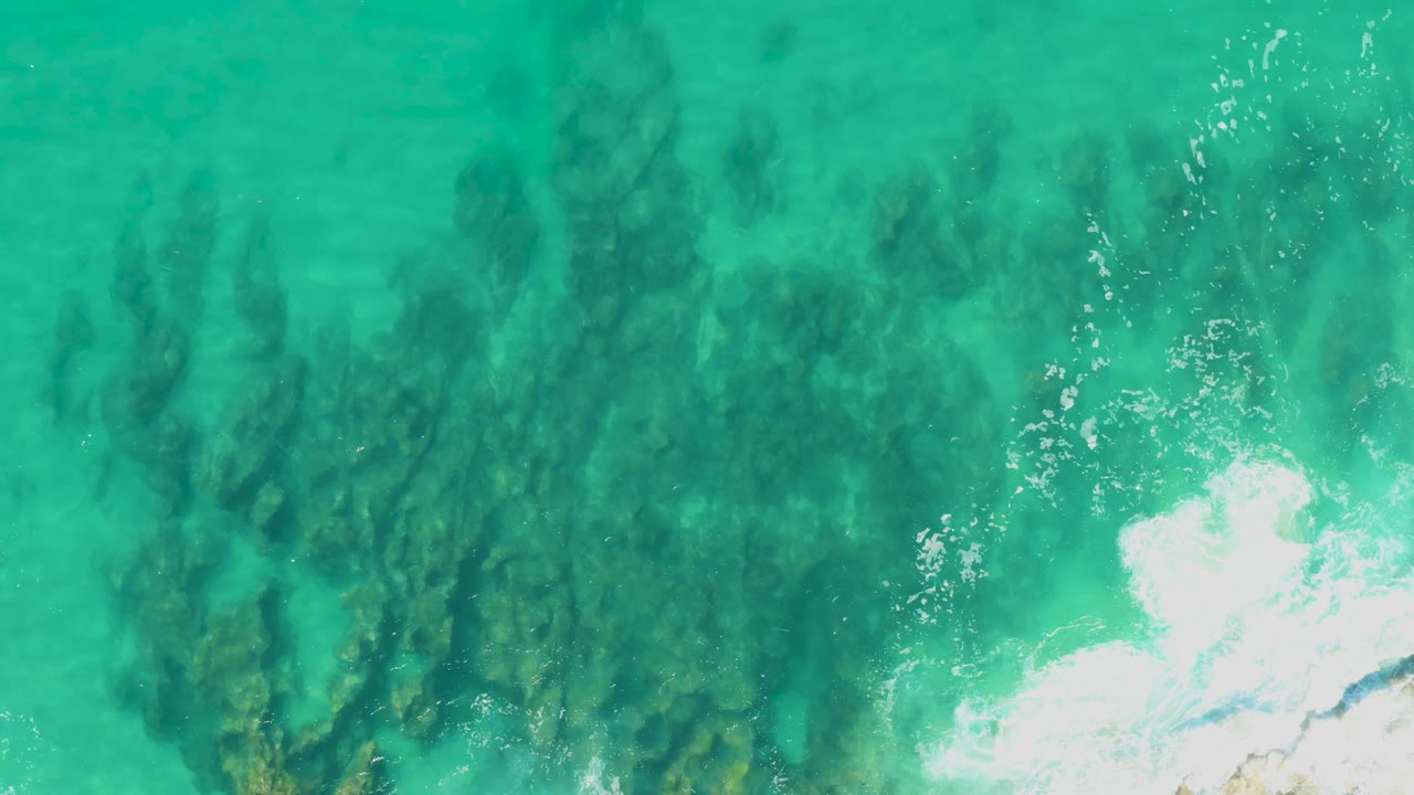 Turquoise shallow water over submerged rocks with foam at the right edge.