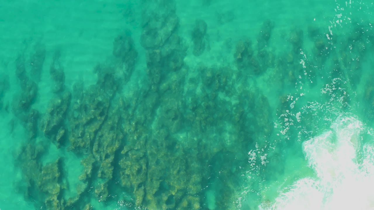 Turquoise water at Laguna Beach Los Cabos covers dark rock ridges, with foamy white water pushing in from the right edge and no visible people.