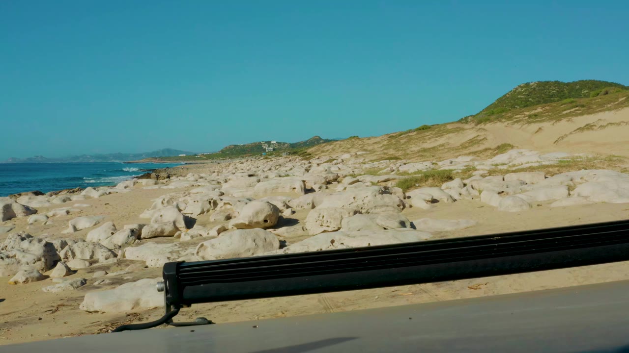 Coastal rocks and sand viewed past a dark vehicle edge