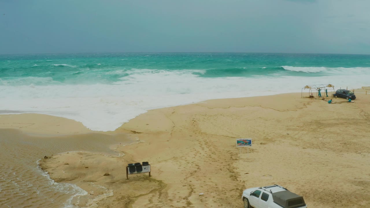 Aerial shot of ocean surf washing onto sand with vehicle at the bottom edge.