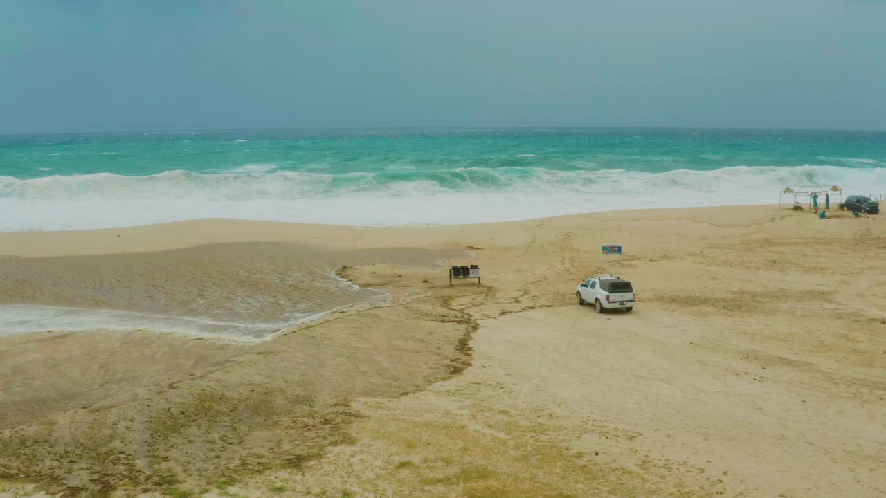 Dreams Resort Los Cabos shoreline view with the white SUV still on the sand as foamy surf spreads farther along the beach, with no visible people.