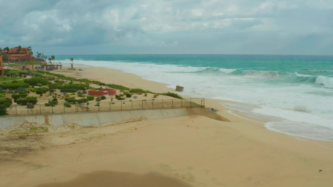 A later view of the Dreams Resort Los Cabos beach shows a fuller band of whitewater across the shore, turquoise water beyond, and no visible people.