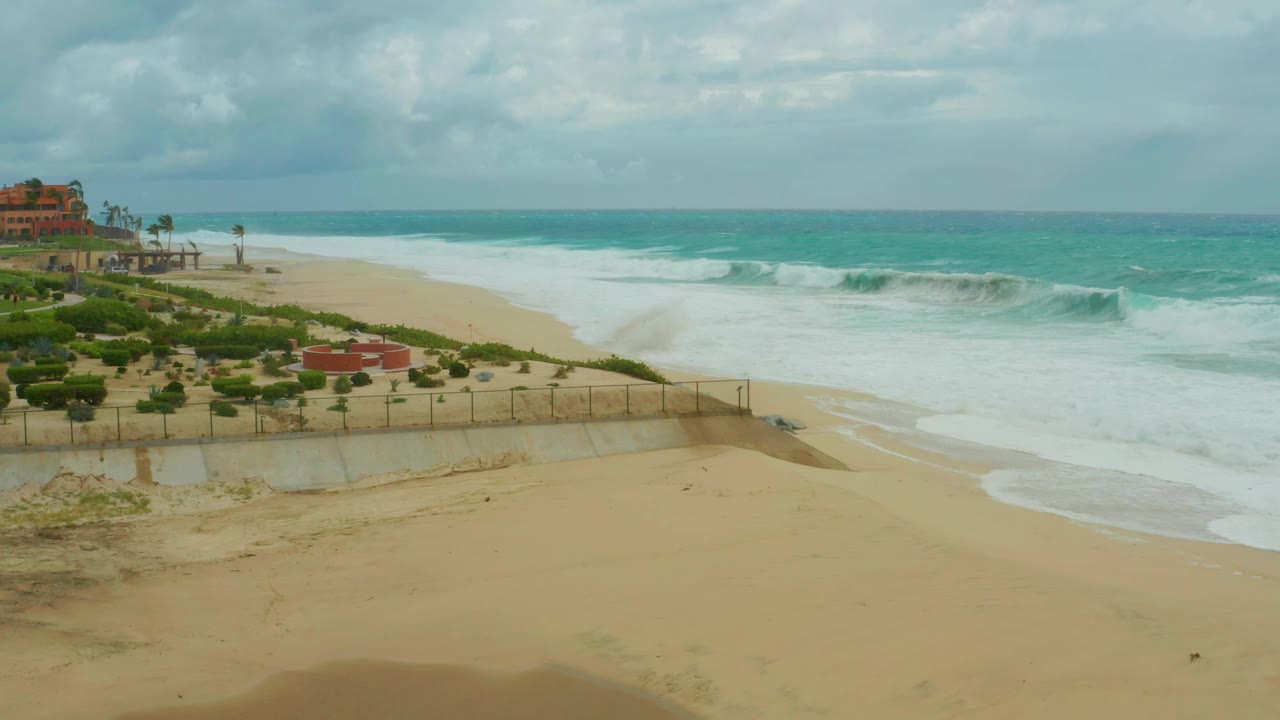 Foamy waves roll toward an empty sandy beach near greenery.