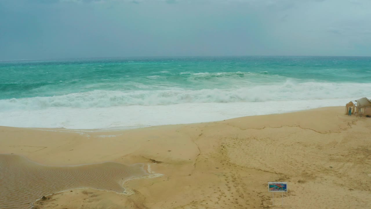 At 0:02, the surf forms a broad white band across the Dreams Resort Los Cabos beach, with a small beach structure near the right edge and no visible people.