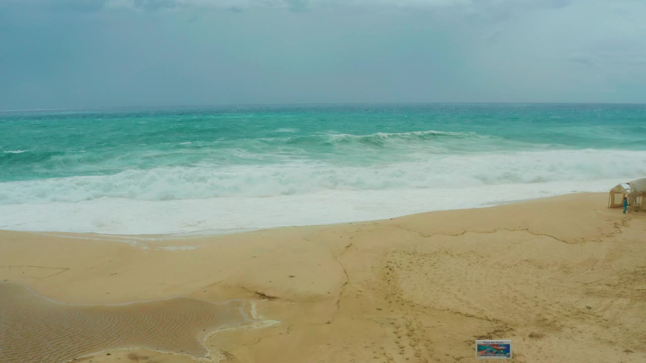 Cloudy sky over waves and sandy beach with structure on right