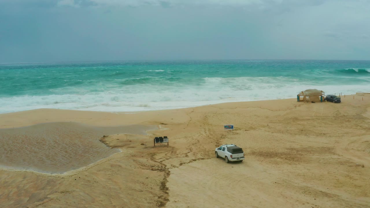 White SUV crosses beach below cloudy sky and surf.