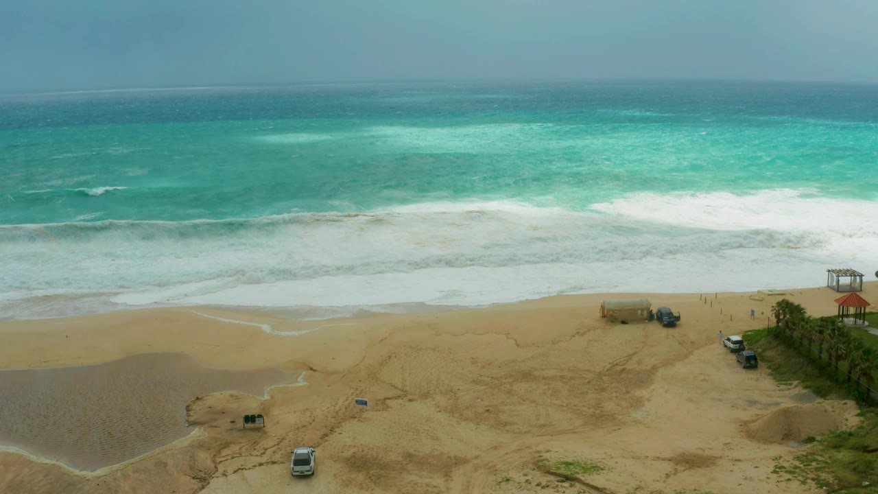 Ocean waves spread white foam across sand near parked beach vehicles.