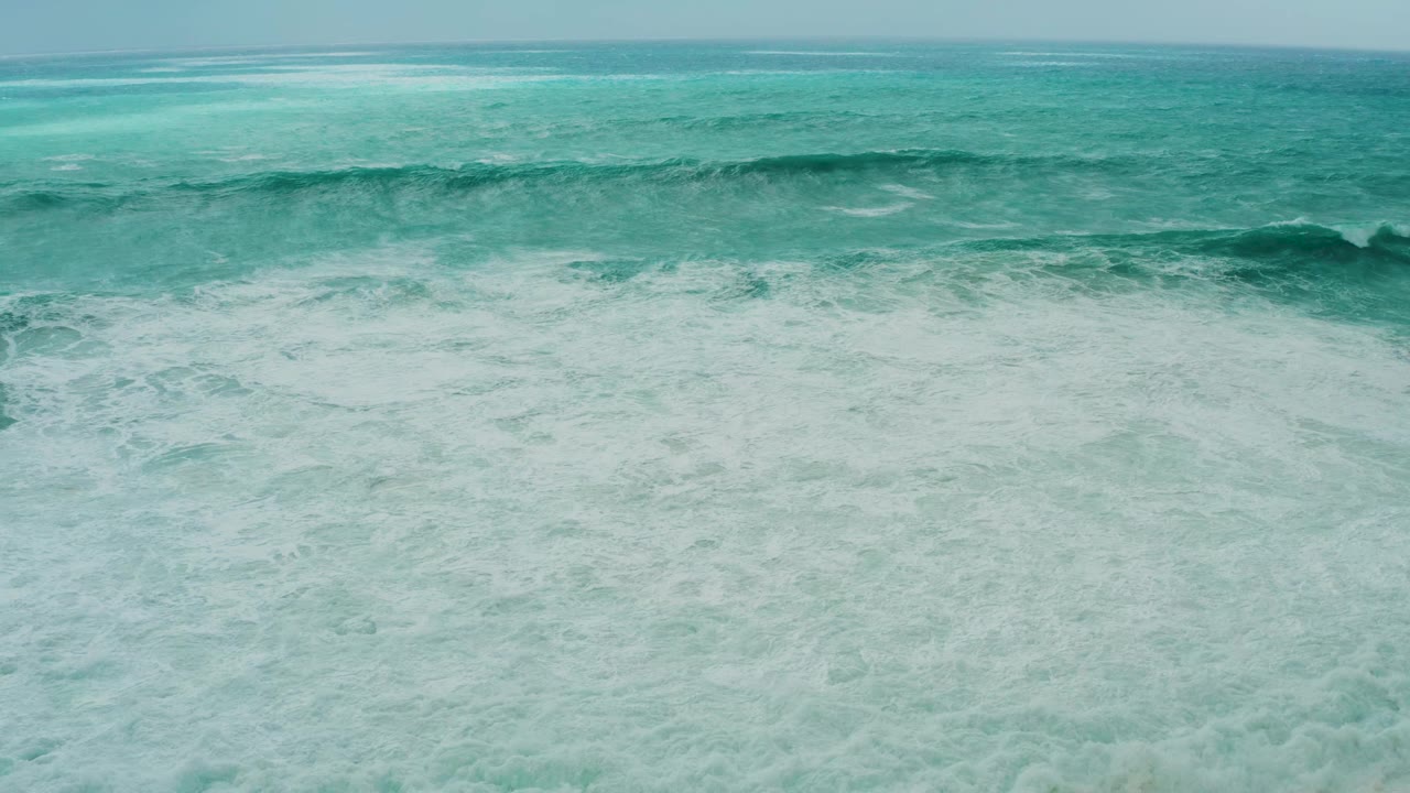 Turquoise ocean with a distant wave line and white foam below.