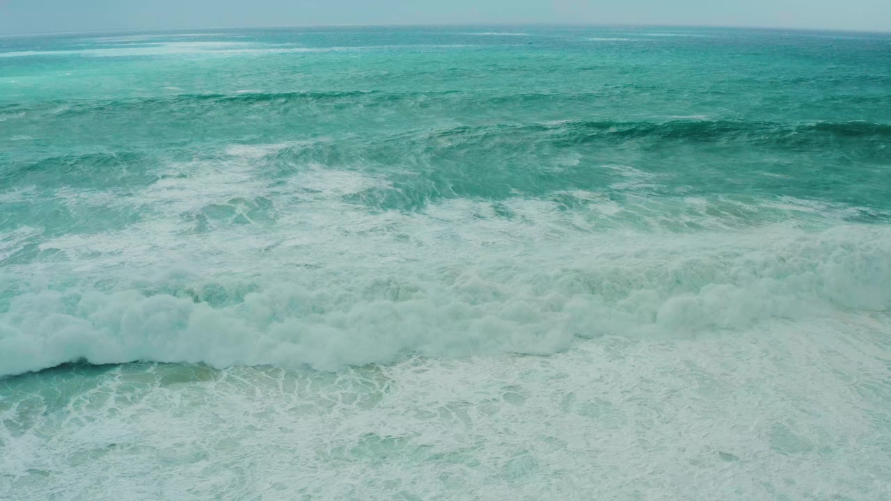 A broad band of whitewater pushes through the center of the Dreams Resort Los Cabos ocean view, with darker teal water beyond and no visible people.