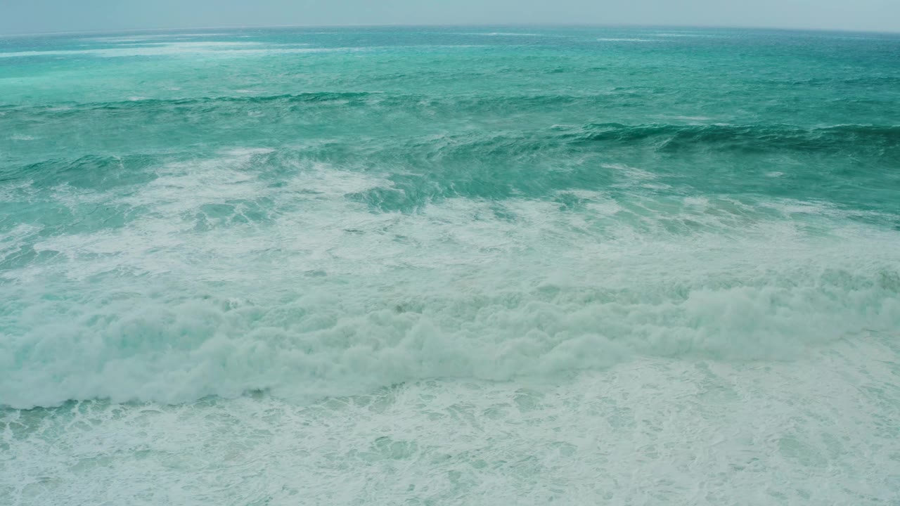 Foamy surf fills the foreground while a darker teal swell forms across the upper middle of the Dreams Resort Los Cabos ocean frame, with no visible people.