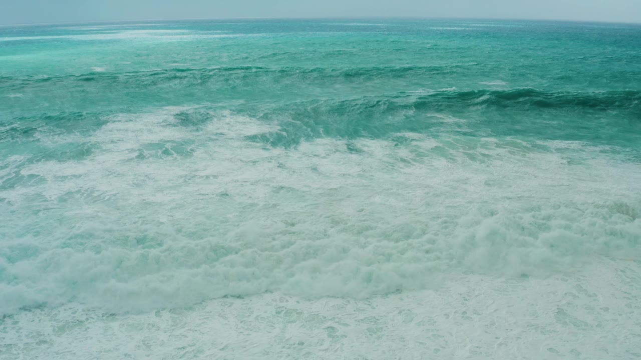 Dense white foam covers the lower half of the Dreams Resort Los Cabos ocean scene, with a turquoise water band and soft horizon above, and no visible people.