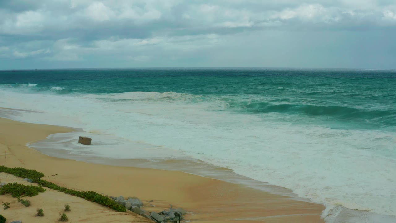 At 0:03, white water spreads across the Dreams Resort Los Cabos beach, with the small rectangular object near the wet sand and no visible people in the frame.