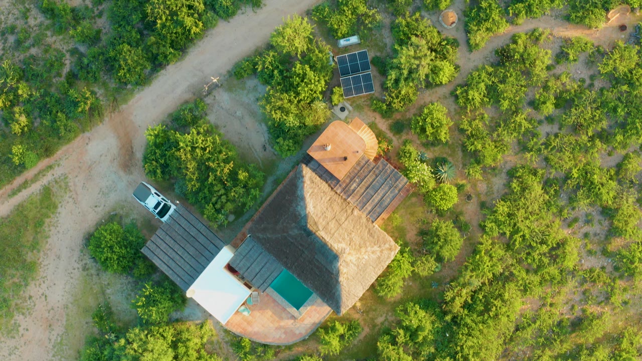 At 0:02, the Cabo Pulmo overhead frame shows the house slightly farther right in the grid cell, with solar panels above it, a dirt road beyond, and no visible people.