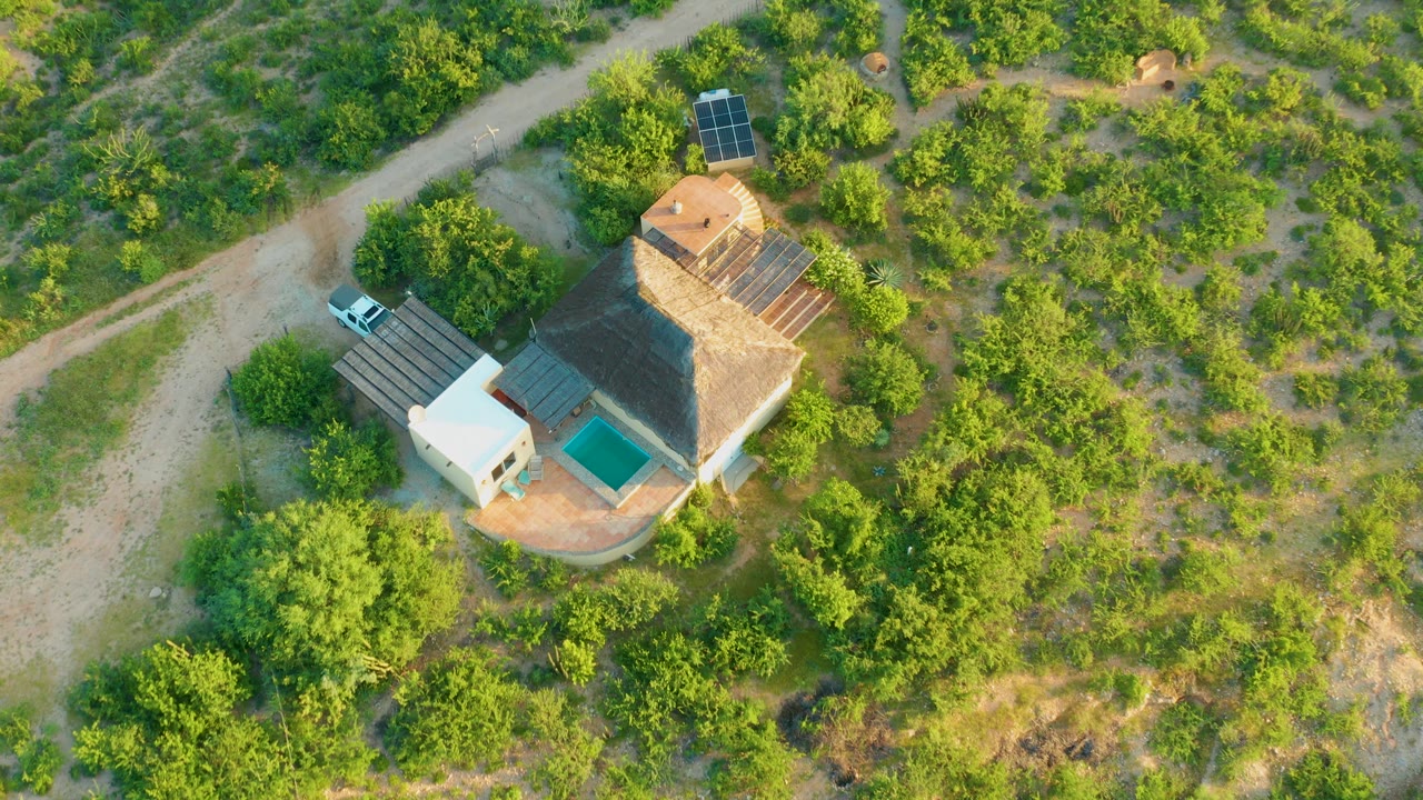 Aerial frame in Cabo Pulmo, Baja California Sur, with the house slightly larger in view, a turquoise pool beside the structure, solar panels nearby, and no visible people.