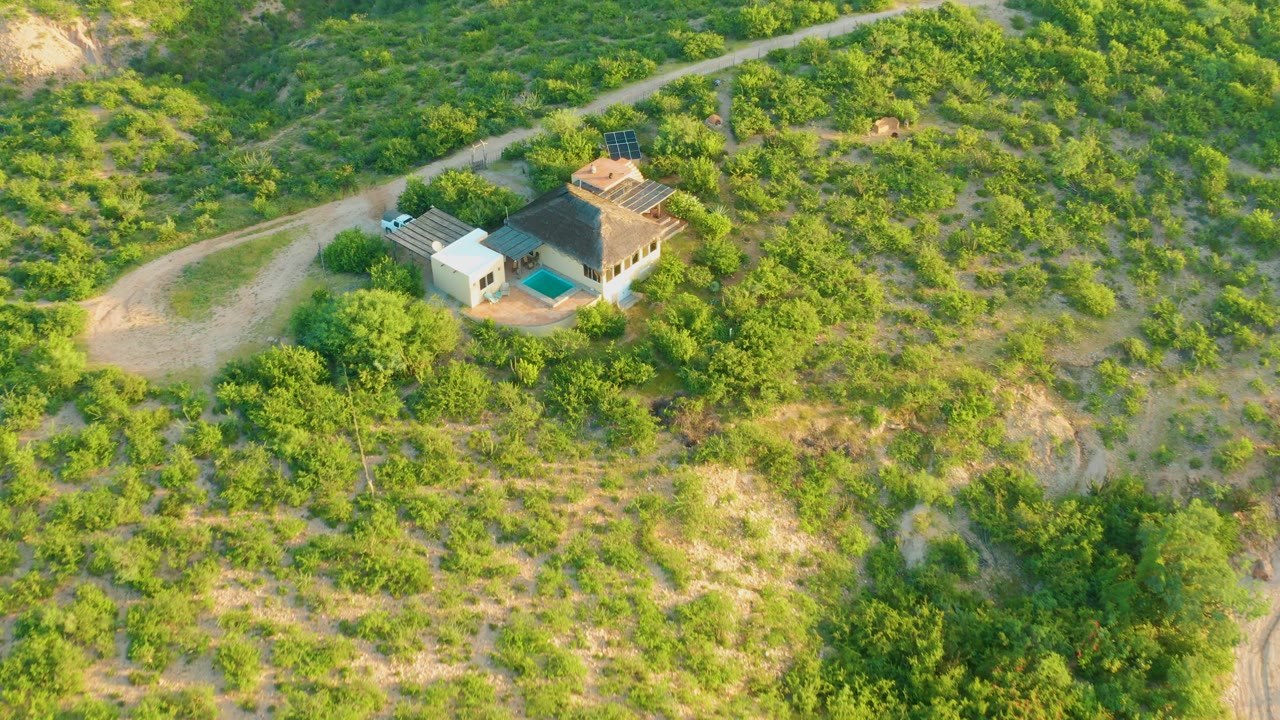 Closer aerial view of a house with a pool and dirt driveway on a green slope