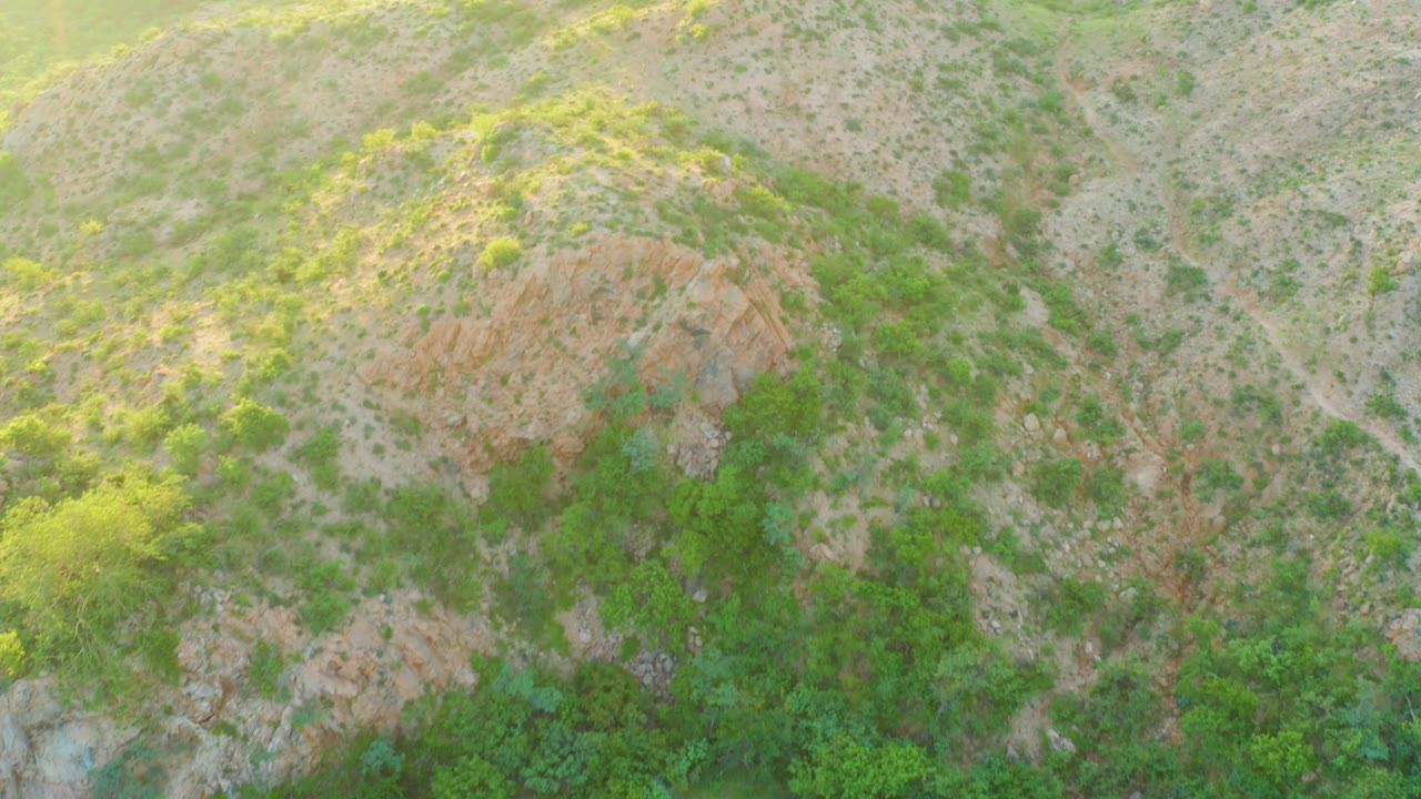 Aerial frame from Cabo Pulmo, Baja California Sur showing a rounded dry ridge, scattered shrubs, small gullies, orange rock, and no visible people.