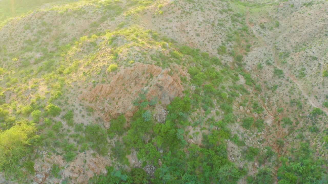 Aerial frame from Cabo Pulmo, Baja California Sur where the hillside shifts across frame, with scrub vegetation, rocky patches, pale soil, and no visible people.