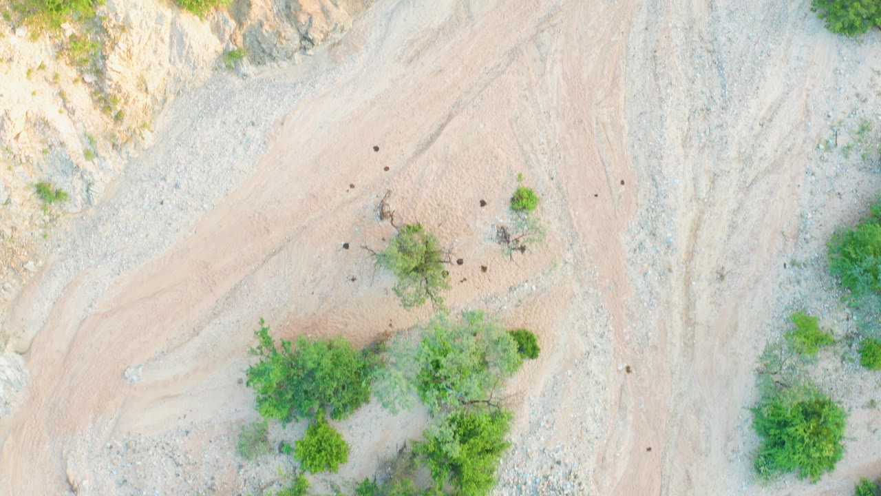 Cabo Pulmo aerial frame showing a tan pathlike dry wash beside pale rocks, scattered green brush, and no visible people.