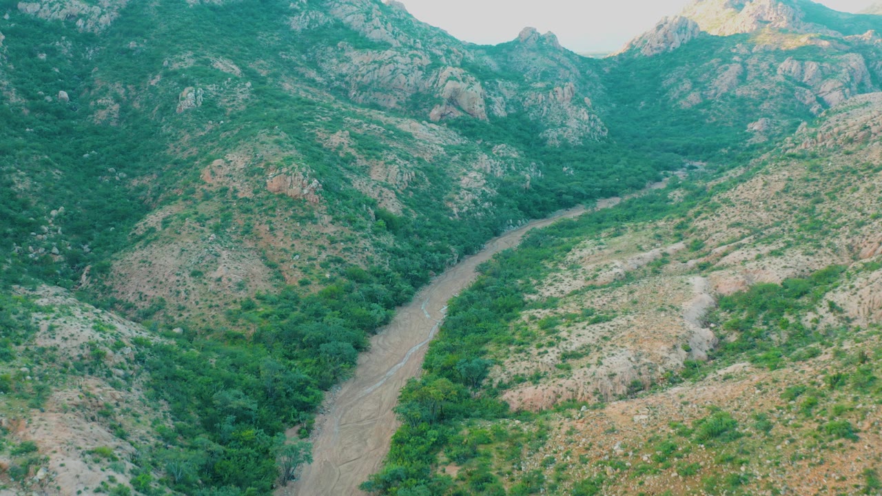 Aerial view of a muddy river winding through a green mountain valley.