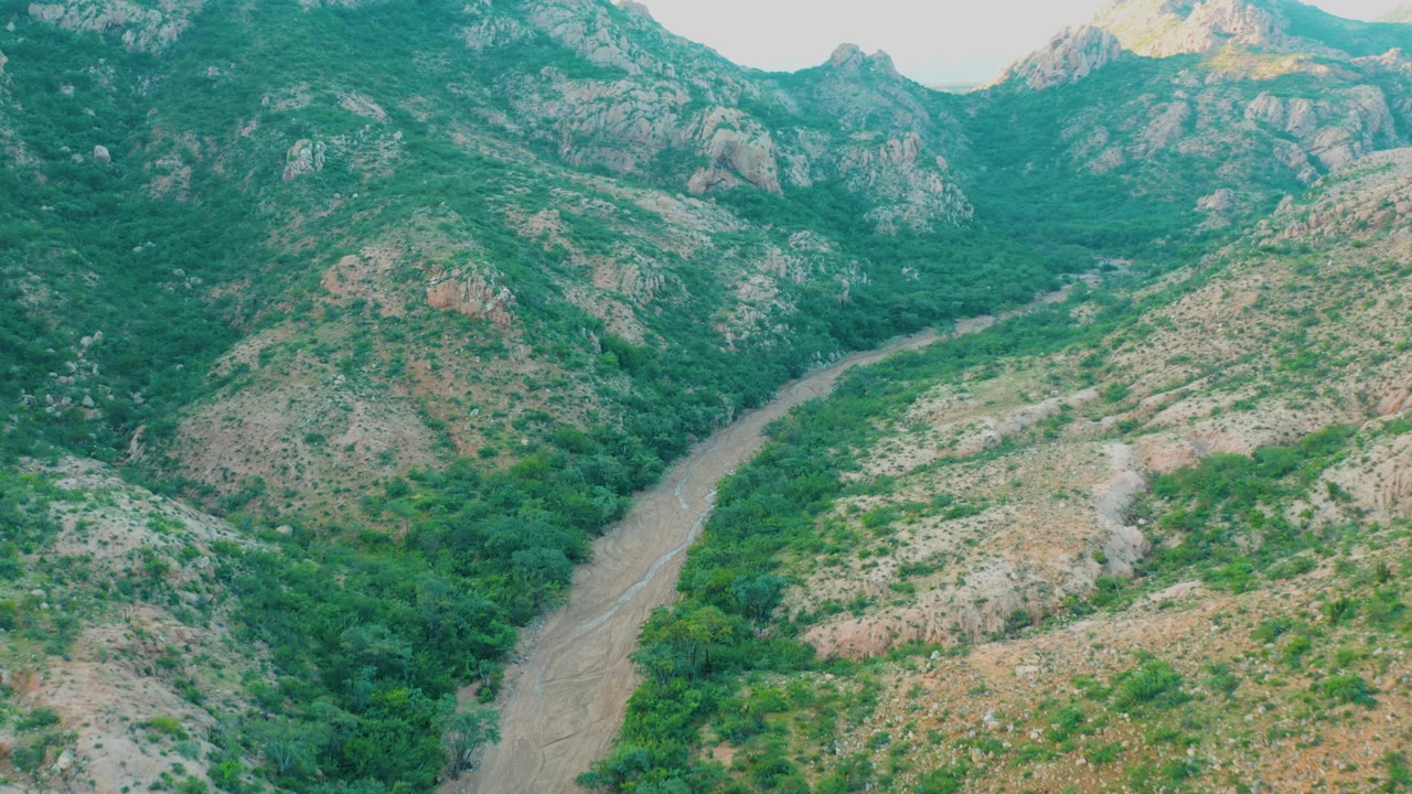 Aerial view in Cabo Pulmo, Baja California Sur, with the river bend slightly farther up the frame between thick green trees and tan rocky terrain, with no visible people.