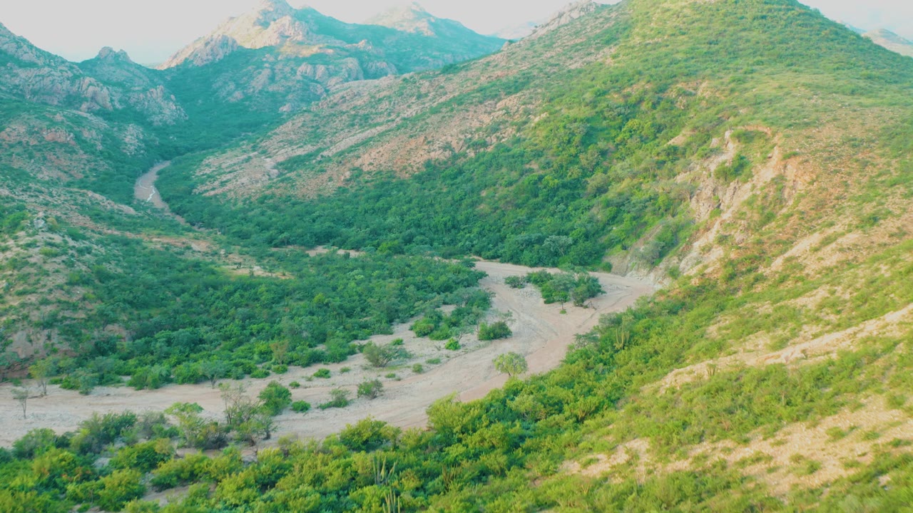 Green valley with a pale dirt road curving between rocky hills.