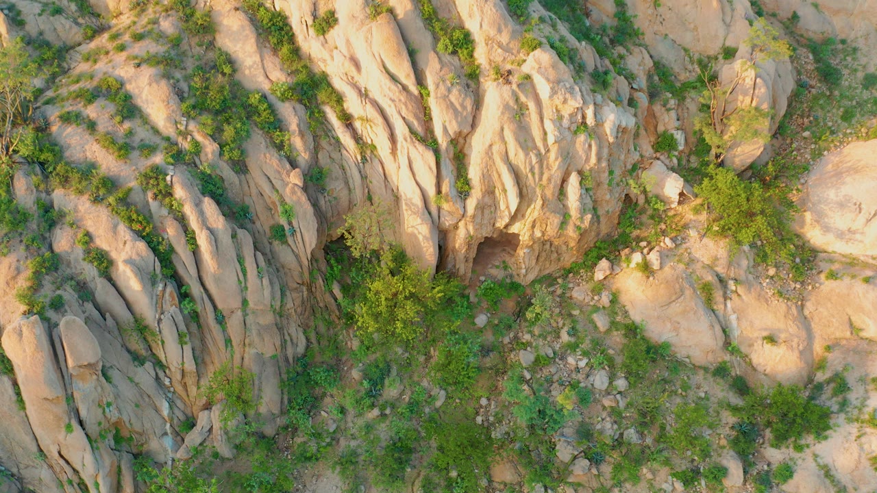 Aerial frame over pale vertical rock grooves, rounded stone slabs, and green brush in Cabo Pulmo, Baja California Sur, with no visible people.