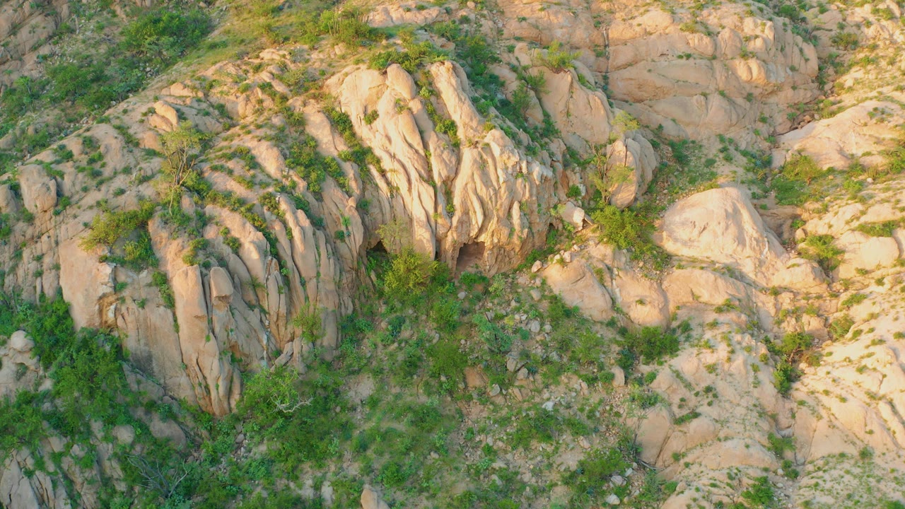 Aerial frame from Cabo Pulmo showing a large central tan rock formation, surrounding scrub, broken ground, and no visible people.