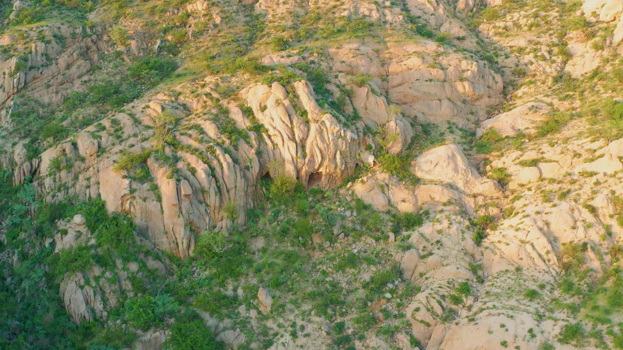 At 0:01, the Cabo Pulmo hillside remains tightly framed on sunlit tan boulders, darker green plant cover, and small shadowed channels with no visible people.