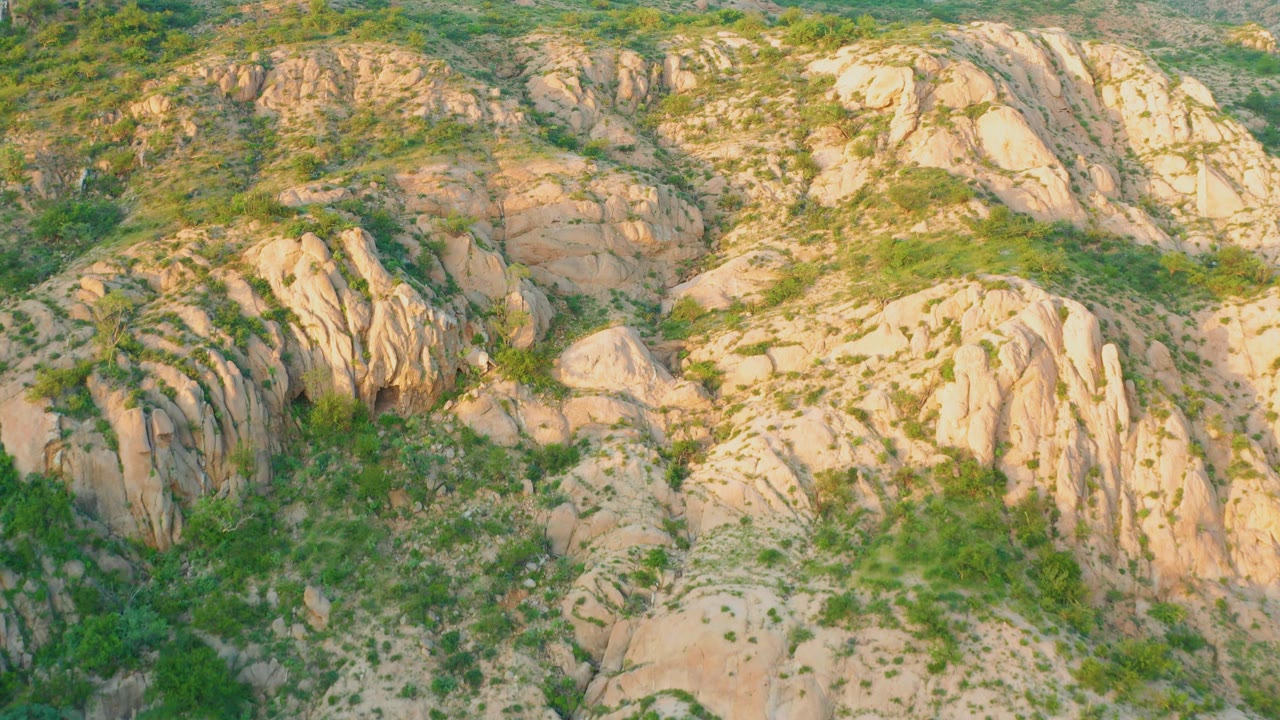 Sunlit tan rock outcrops and green plant cover spread across dry hillside terrain in Cabo Pulmo, with no visible people.