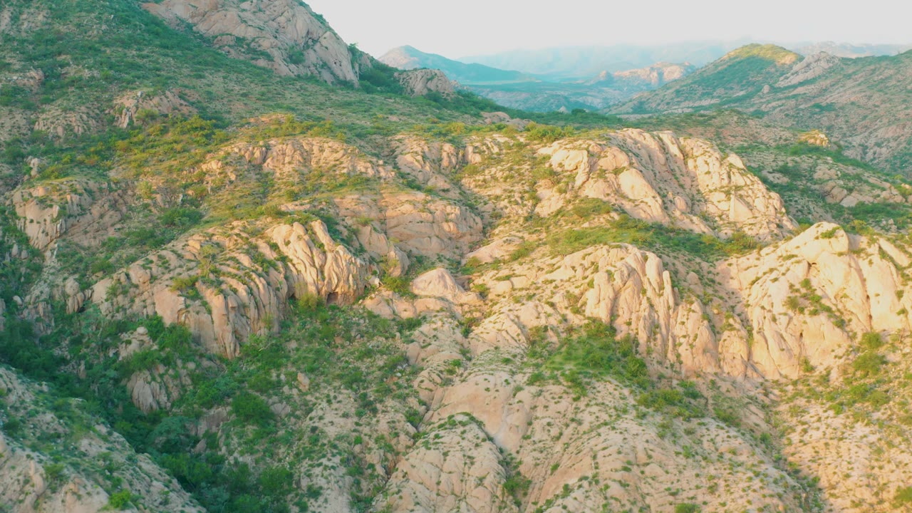 Second frame in Cabo Pulmo shows the same rocky hillside slightly shifted, with bright tan rock faces, green brush patches, distant hazy hills, and no visible people.