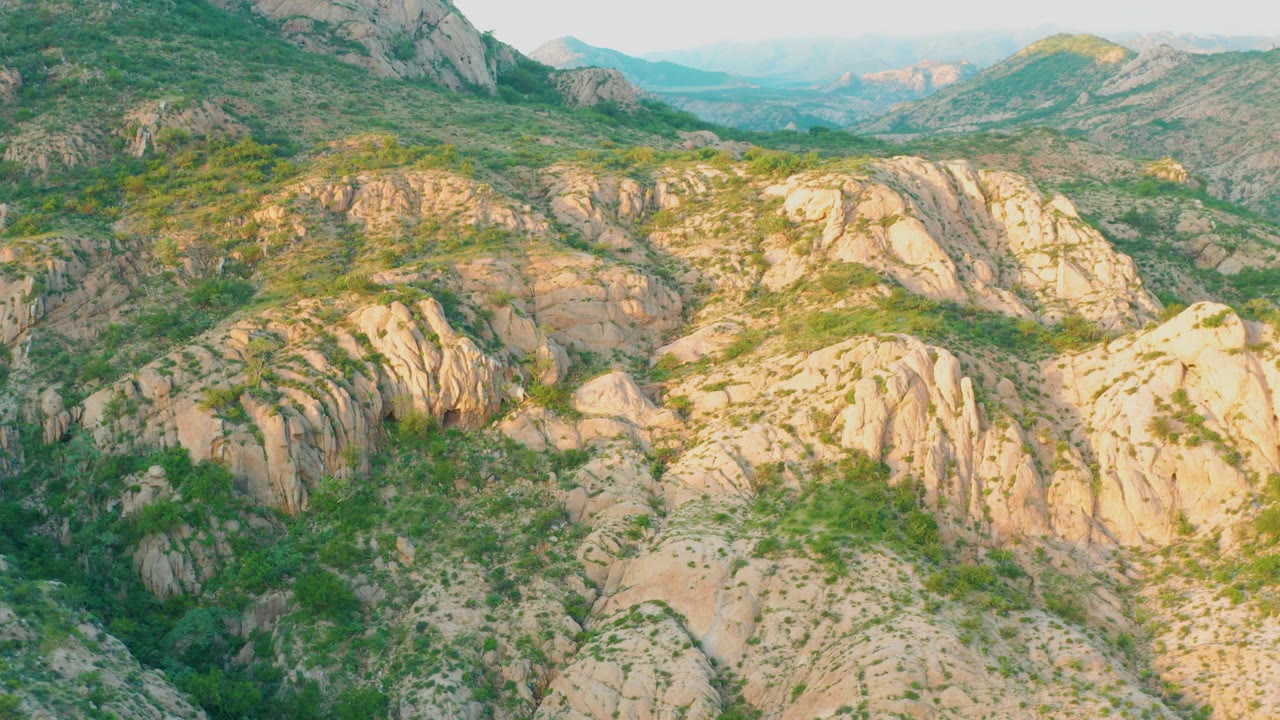 Mid-clip frame over Cabo Pulmo mountain terrain, where pale boulder ridges dominate the lower frame, green scrub breaks up the rock, and no visible people appear.