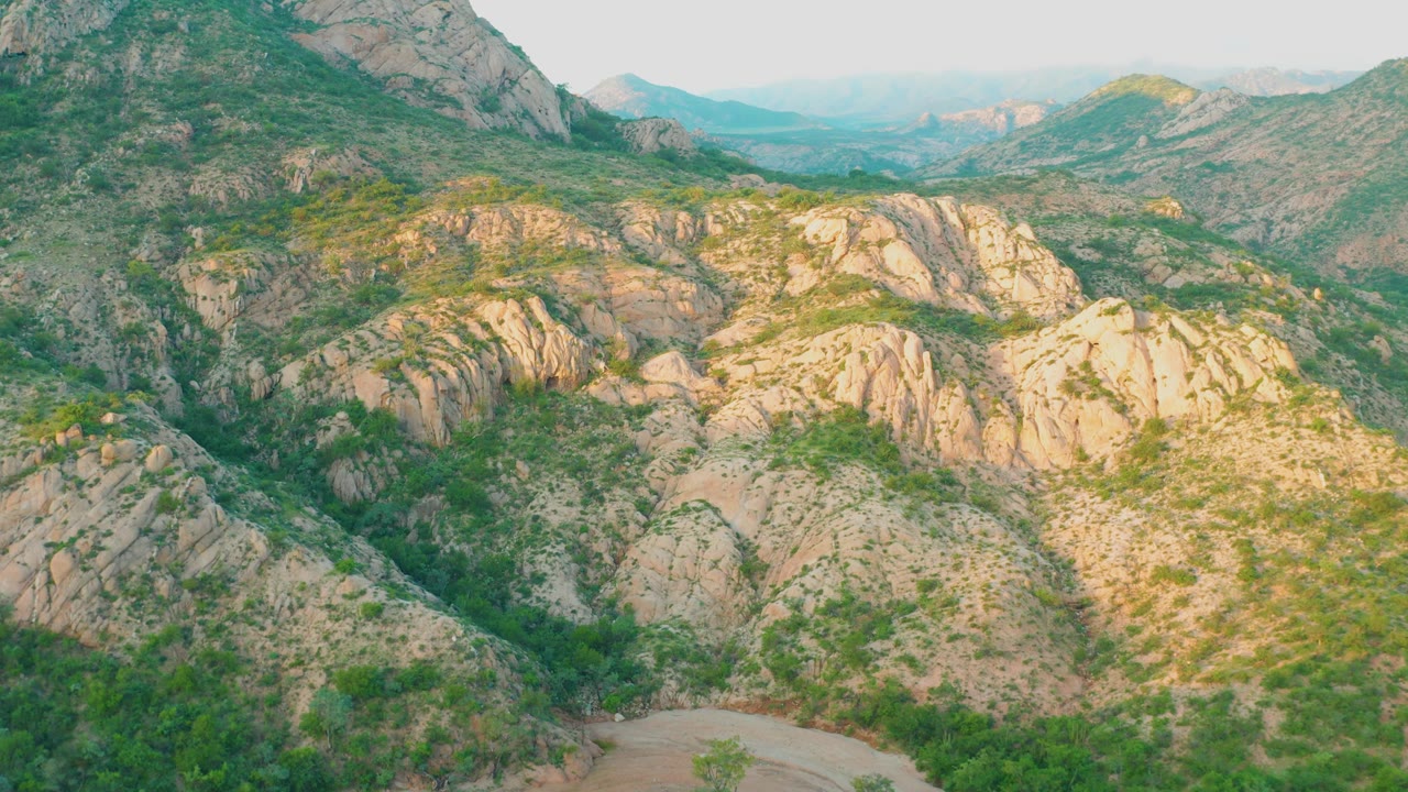 Aerial view in Cabo Pulmo with the rocky ridge filling the center, green vegetation in gullies, pale sunlit stone on the right, distant hills, and no visible people.