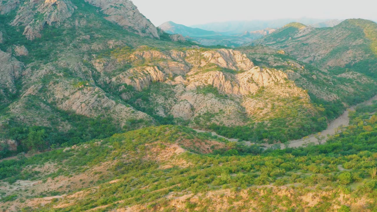 Aerial frame at 0:01 over Cabo Pulmo, Baja California Sur, showing the river tucked below green vegetation and sunlit rock bands, with no visible people.
