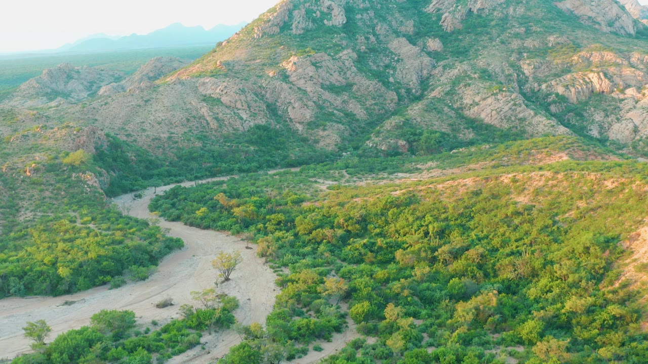 Winding pale riverbed through green valley below rocky mountains