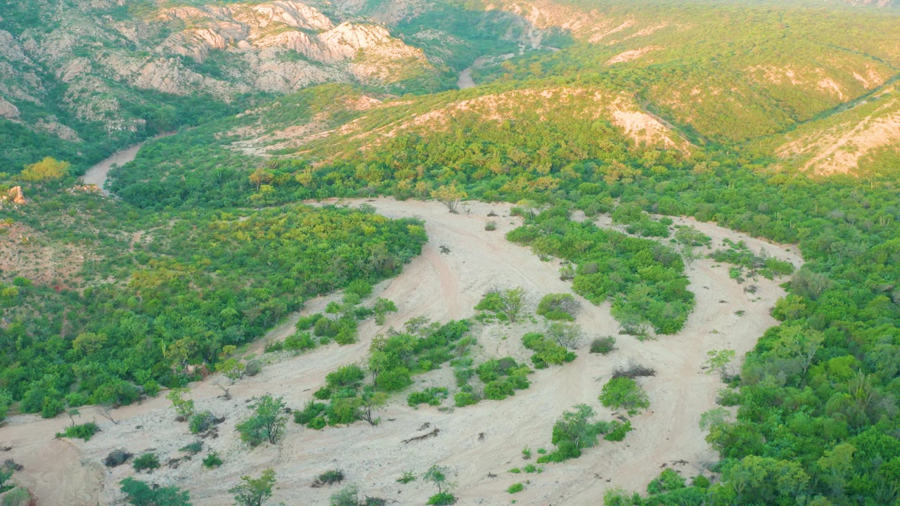 Aerial landscape with dry wash, green vegetation, and rocky hills.