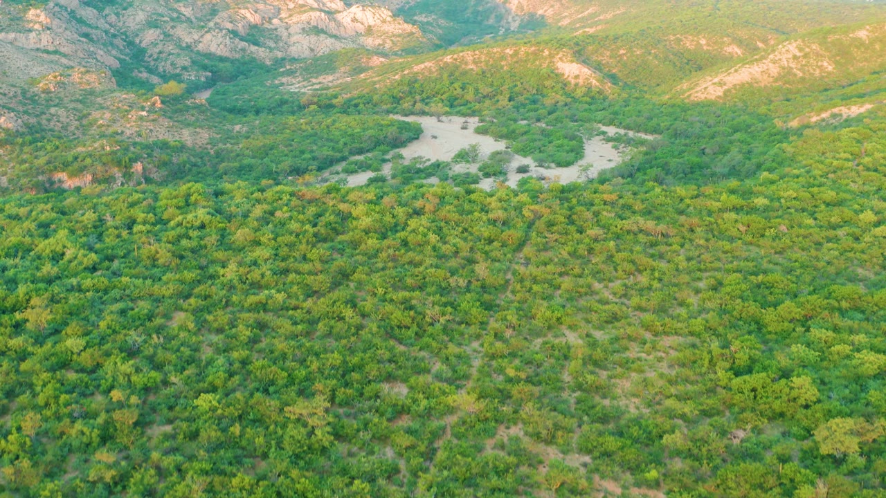 Aerial frame from Cabo Pulmo, Baja California Sur, Mexico, showing the river channel set back in a green valley, with layered mountain ridges and no visible people.