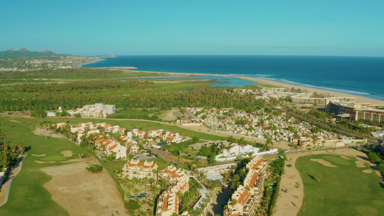 Drone view across golf course, homes, palms, beach, lagoon-like water, and ocean.