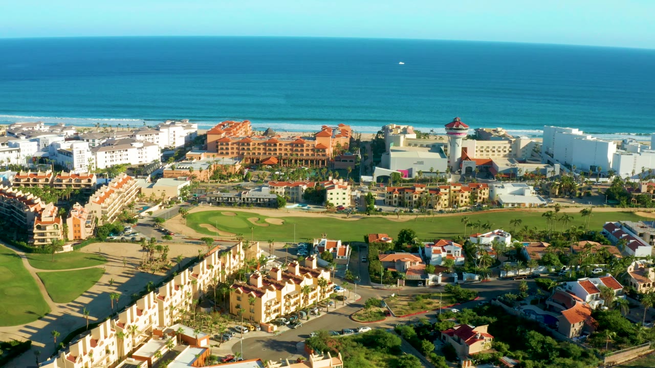 Wide drone view of oceanfront buildings and green grounds.