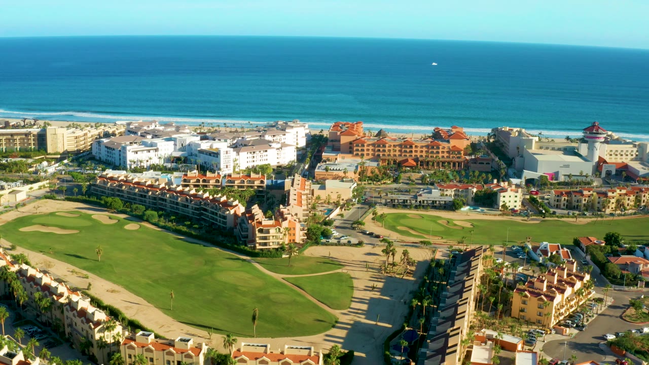 Coastal aerial with golf course foreground and ocean horizon behind buildings.