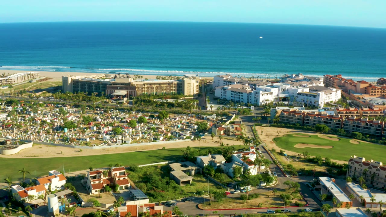 Aerial view across ocean, beach, hotels, residential buildings, and field.