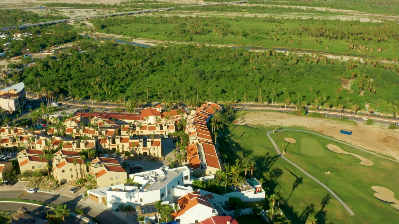 Overhead view of red-tile residences, a road, and golf course grass.